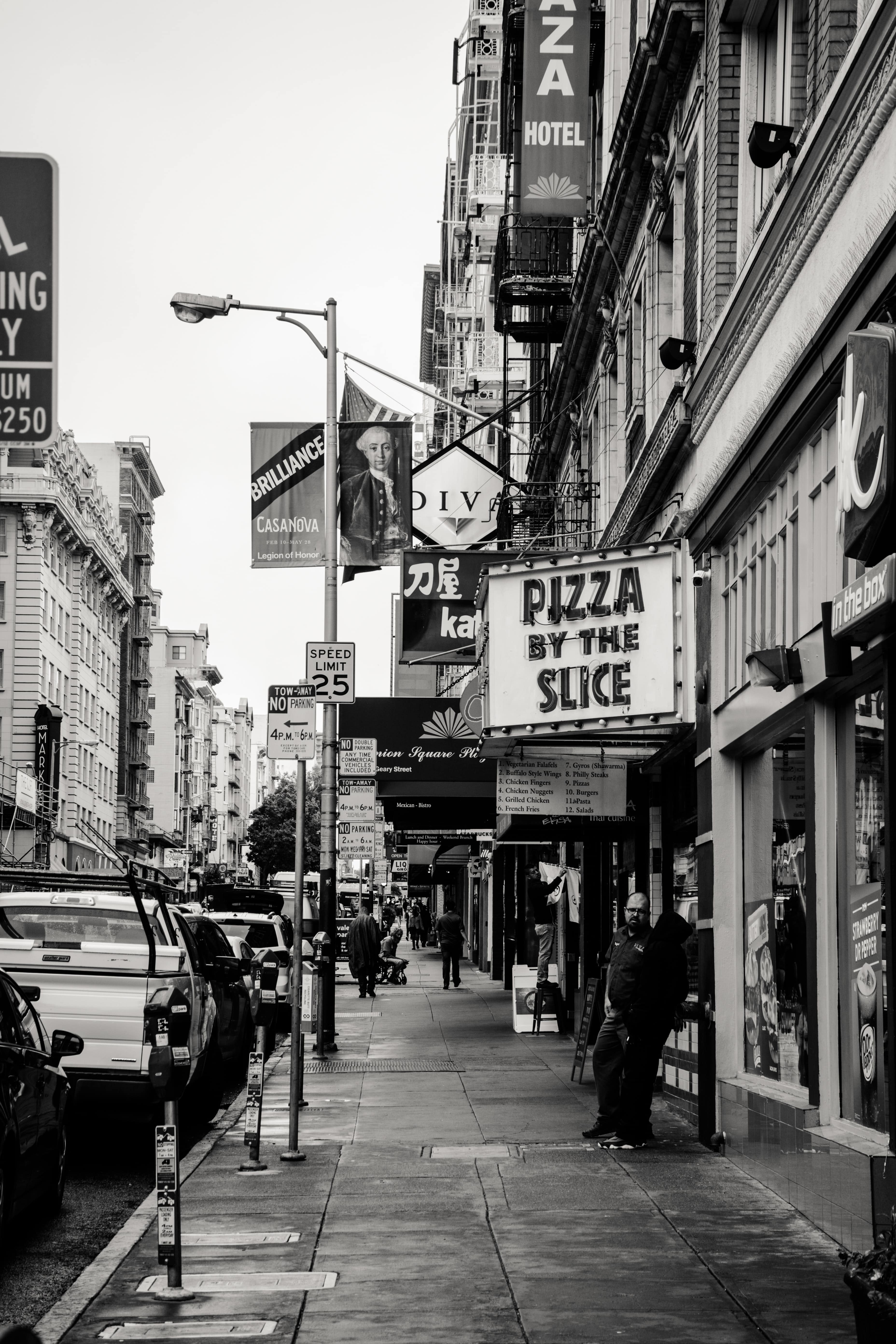 CIty street with a sign that reads "pizza by the slice"